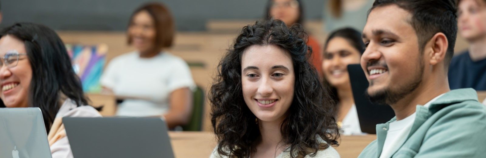 Two students looking at a laptop in a busy lecture theatre.
