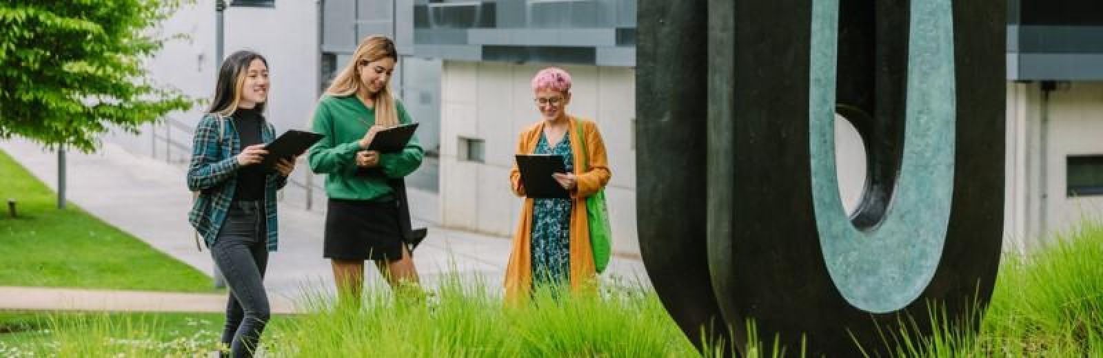 Three students hold ipads, looking at a sculpture on campus.
