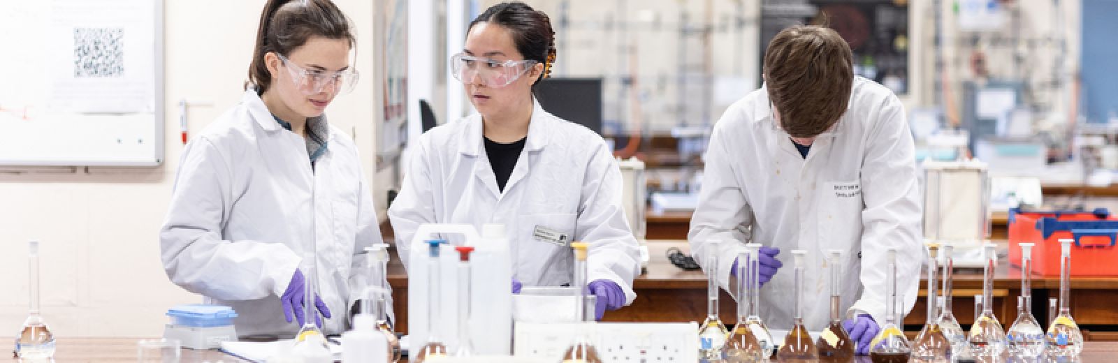 two female students and one male student doing experiments in the chemistry lab