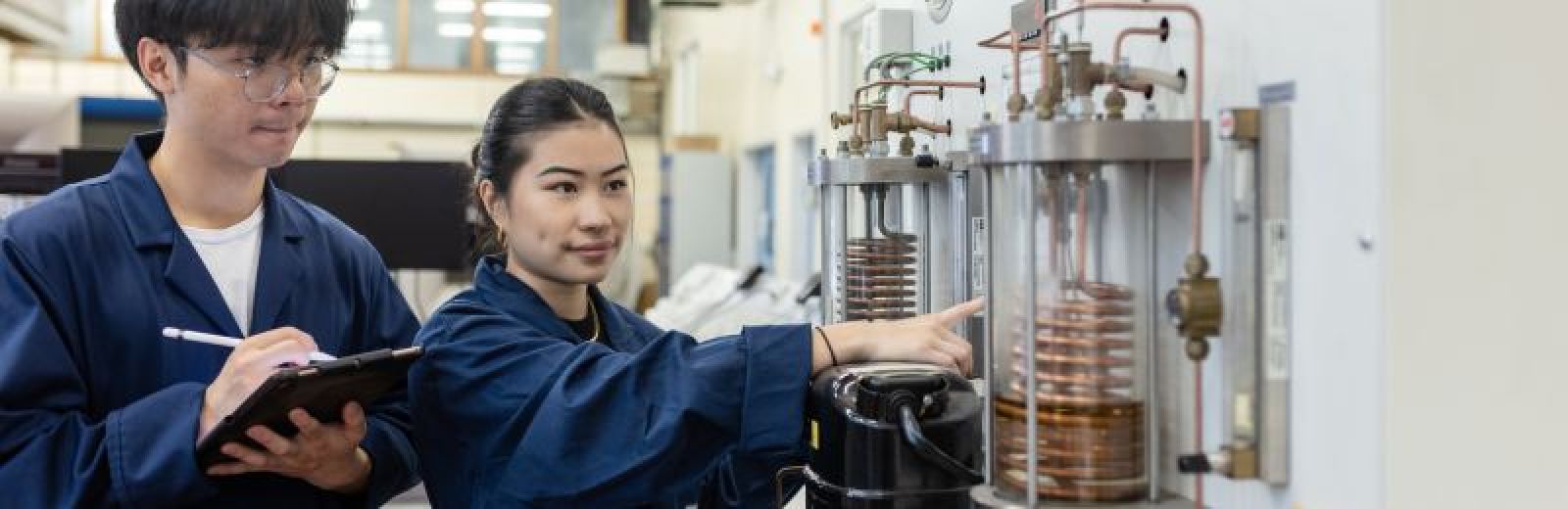 Two students working on a refrigeration machine in a mechanical engineering workshop.