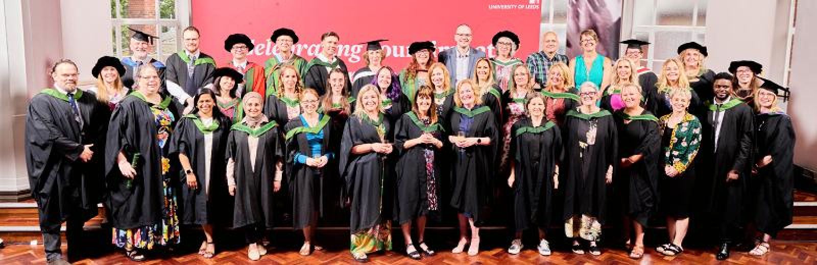 Multiple students in graduation robes and hats stand in front of a red screen.