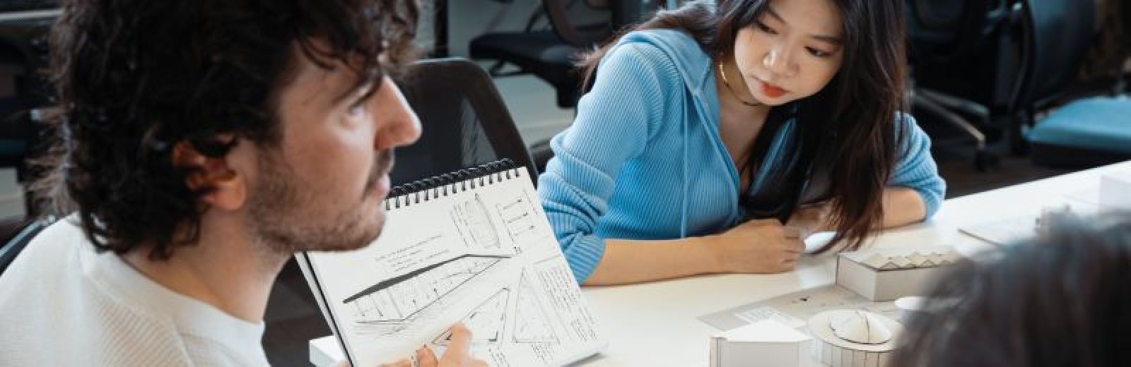 Image of students working in the design studio looking at a sketch book and model buildings.